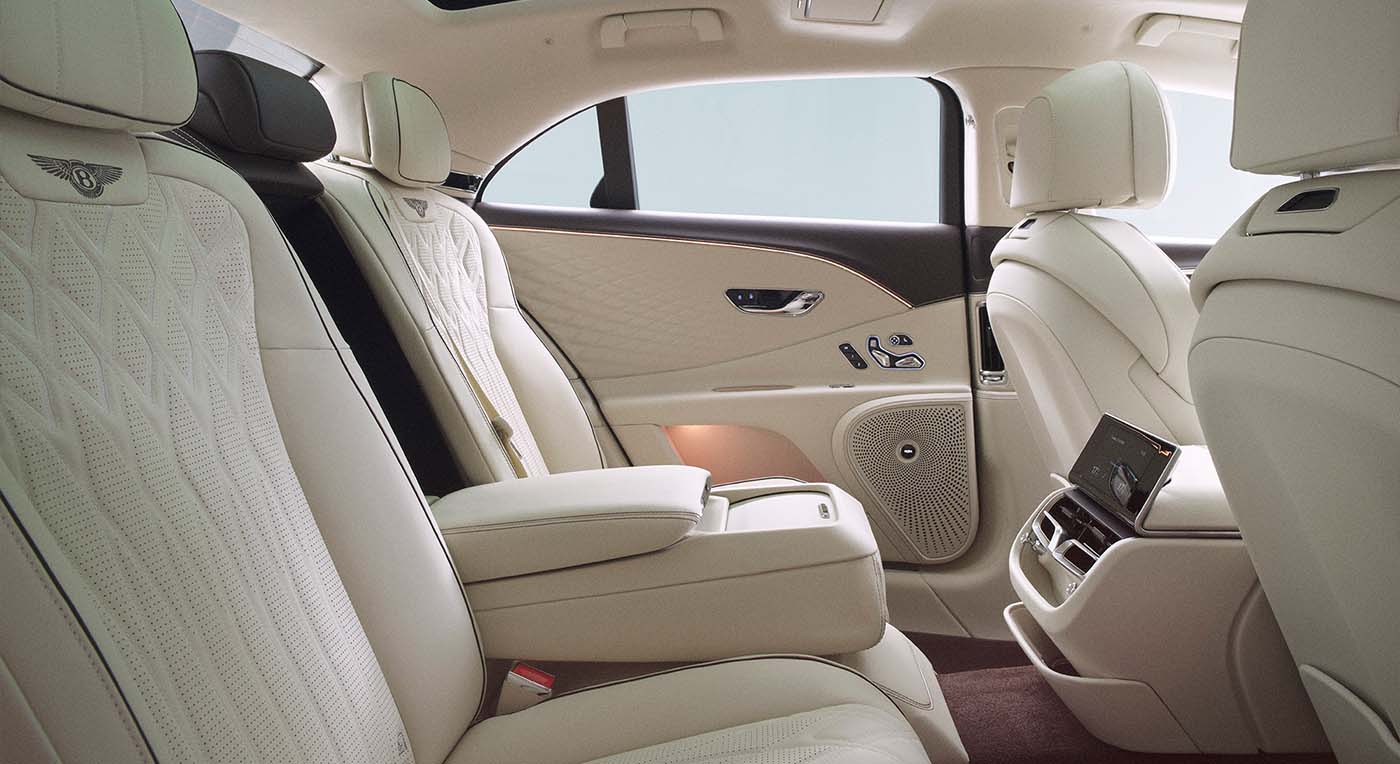 Luxurious Bentley Spur car interior with white quilted leather seats, plush armrest, digital screen, and ambient lighting, conveying elegance and comfort.